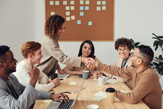 Team gathered around a conference table, where two people are shaking hands across the table.