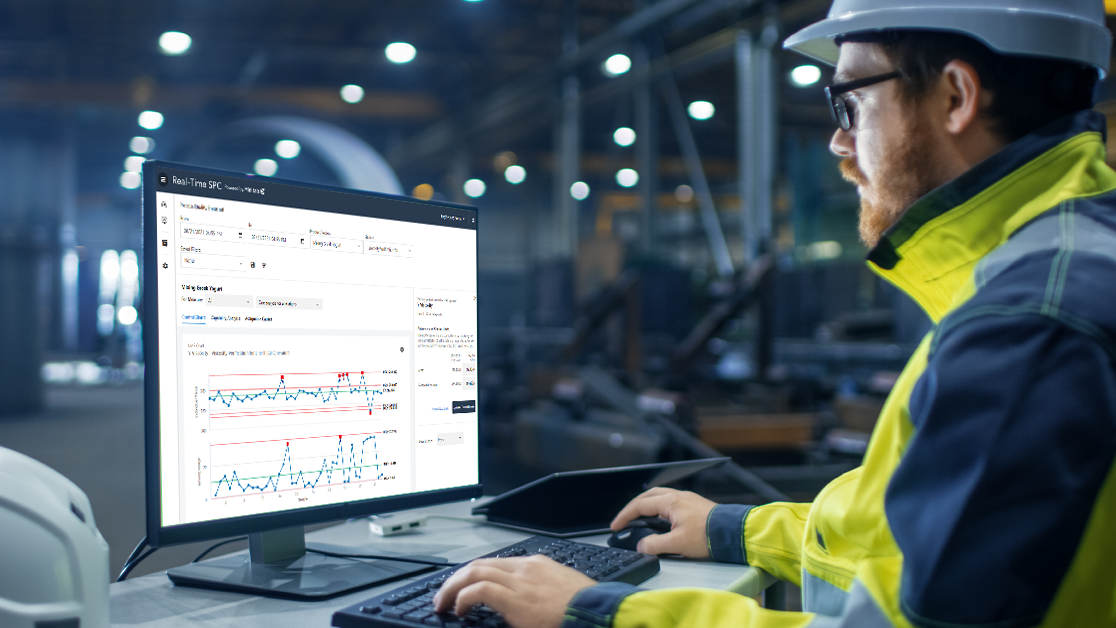 Engineer in a hardhat and vest analyzing statistical process control charts on a computer in a factory.