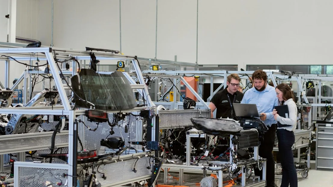 Two men and a woman standing around a computer in an automotive manufacturing warehouse analyzing FMEAs.