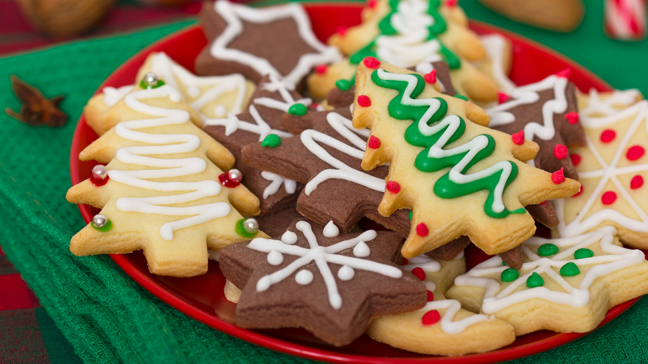 緑のテーブルクロスの上に、飾り付けたクリスマスクッキーが一杯の赤い皿。
